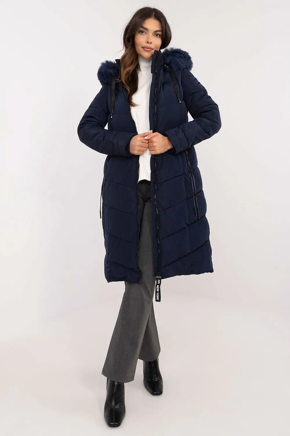 Woman wearing navy long quilted down jacket with detachable fur hood and zipper pockets.