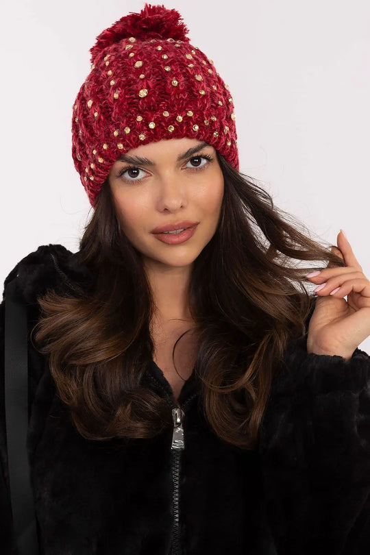 Woman wearing red winter beanie with pom-pom and zircon details, styled for warmth and elegance
