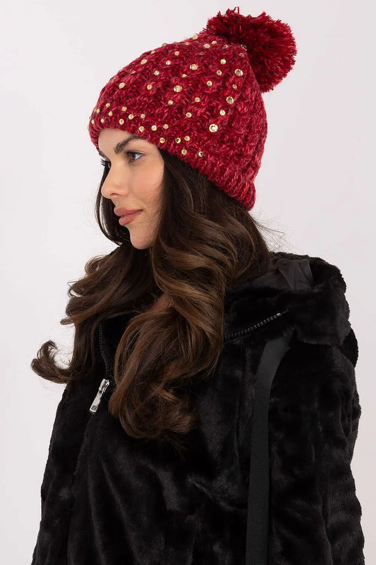 Woman wearing a red winter beanie with pom-pom and zircon details, styled with a black fur jacket