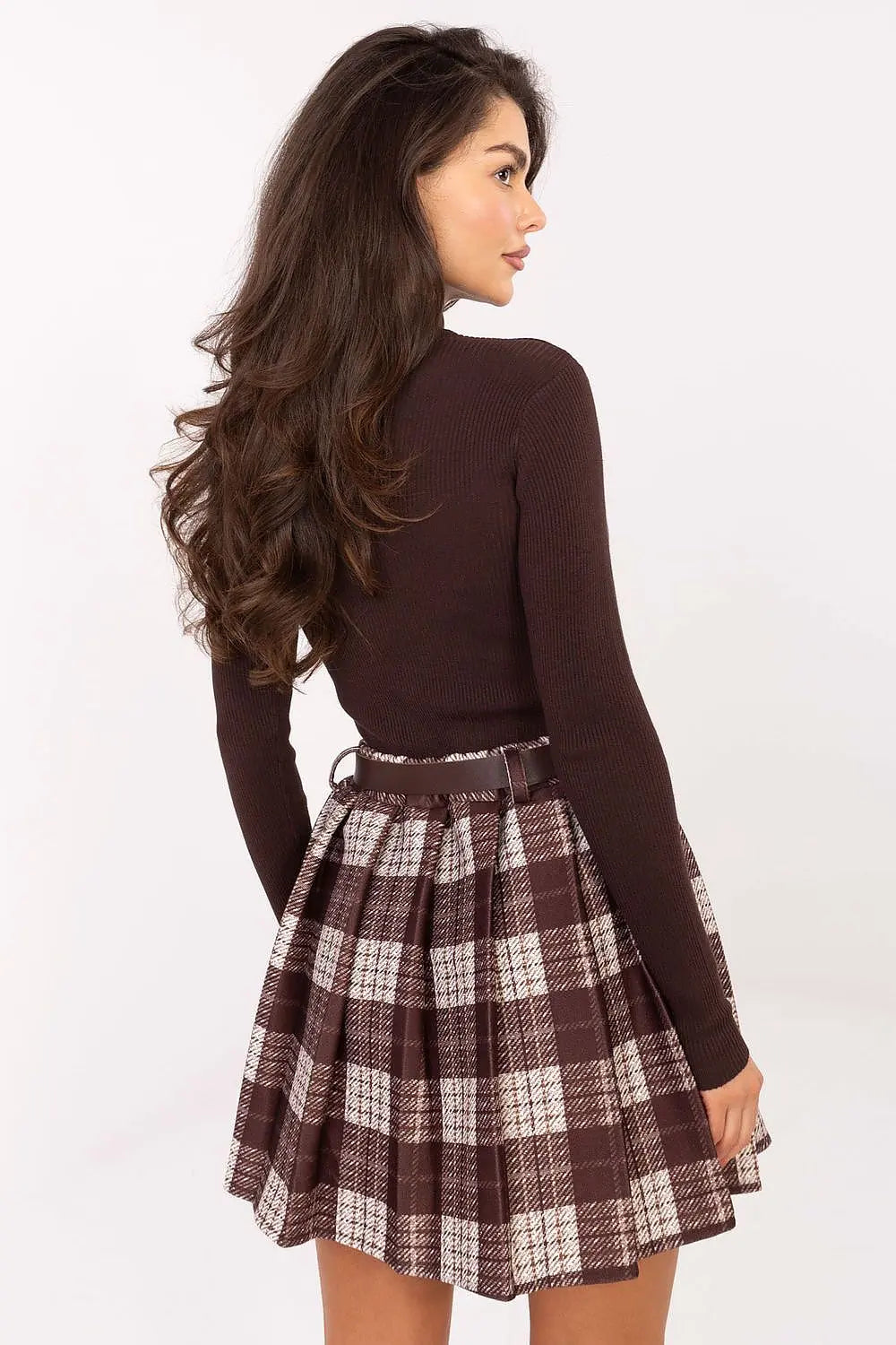 Woman wearing a pleated checkered short skirt with belt and brown top, back view