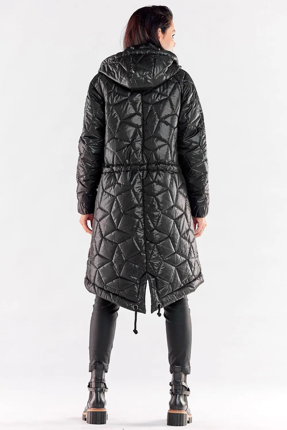 Back view of a black women’s long quilted hooded jacket with drawstring waist and extended back, worn with black pants and boots.