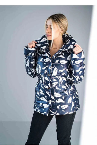 Woman wearing a navy blue shiny quilted jacket with white leaf pattern and high collar