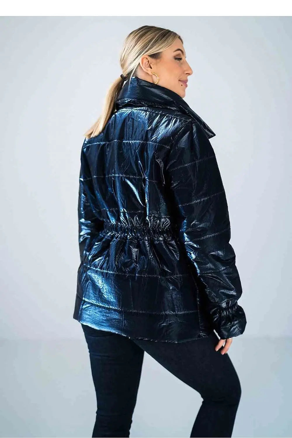Back view of woman wearing shiny quilted hip-length jacket with high collar and elastic waist detailing