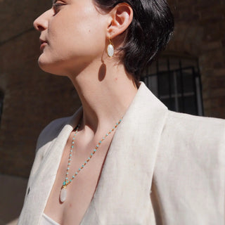 Charis Oval Gemstone Earrings featuring Pariba Onyx set in 22K gold on recycled brass, worn by a woman in a beige blazer.