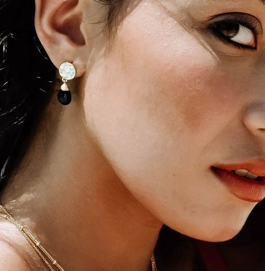 Close-up of Classic Athena Drop Earrings featuring black onyx gemstone set in 22 karat gold on recycled brass, worn on a woman's ear
