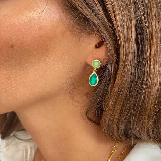 Close-up of gold double gemstone drop earrings featuring green onyx and prenite worn by a woman