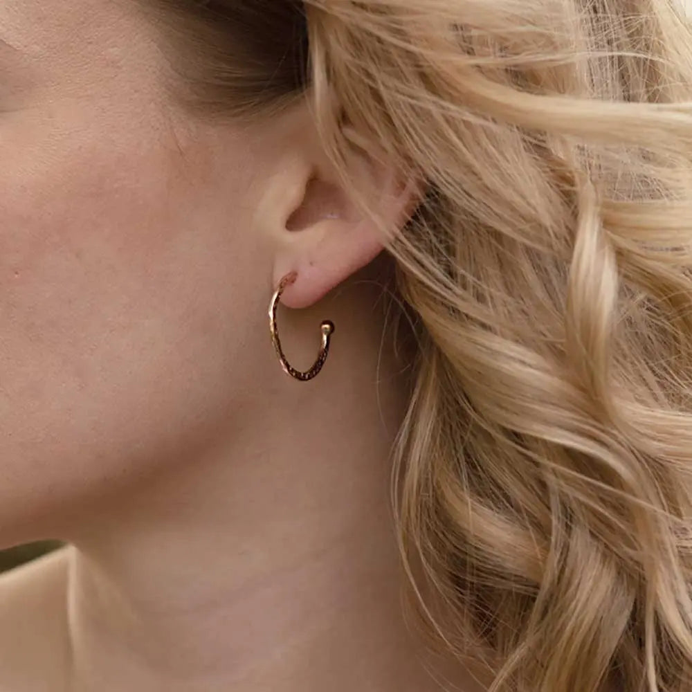 Close-up of a woman wearing Lydia Textured Gold Hoops earrings with a handcrafted textured finish, 22mm 22kt gold plated recycled brass hoops