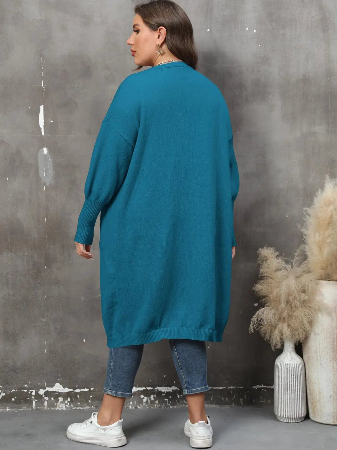 Plus size long sleeve teal cardigan with ribbed texture and pockets, worn with denim jeans and white sneakers, shown from back