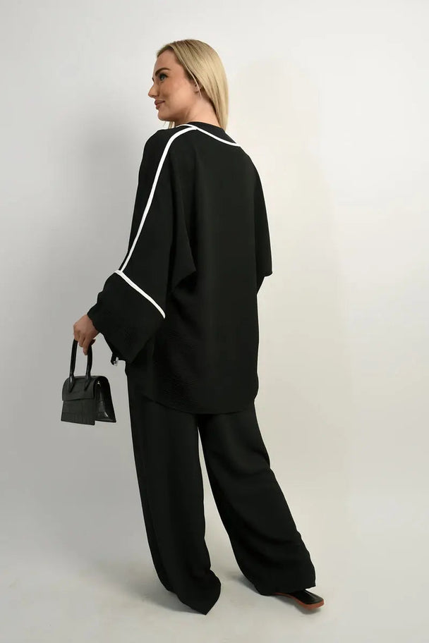 Woman wearing black contrast trim oversized cardigan and wide leg co-ord set carrying a small black handbag facing sideways