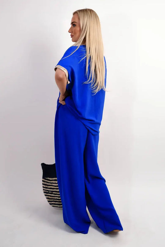 Woman wearing blue wide leg trousers with shiny drawstring waist facing sideways