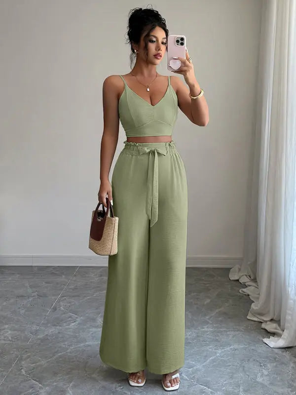 Woman wearing green suspender vest with wide leg pants two-piece set holding a handbag and taking a mirror selfie
