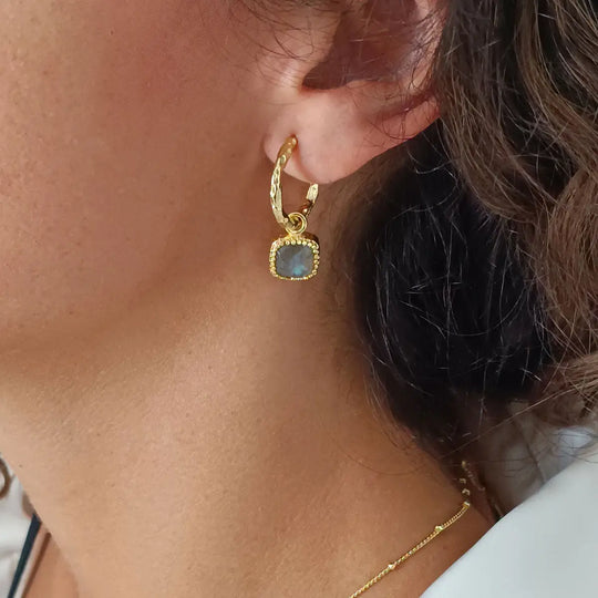 Close-up of a woman's ear wearing 22K gold textured hoop earrings with Labradorite square gemstone charm Tetra Square Gemstone Charm Hoops